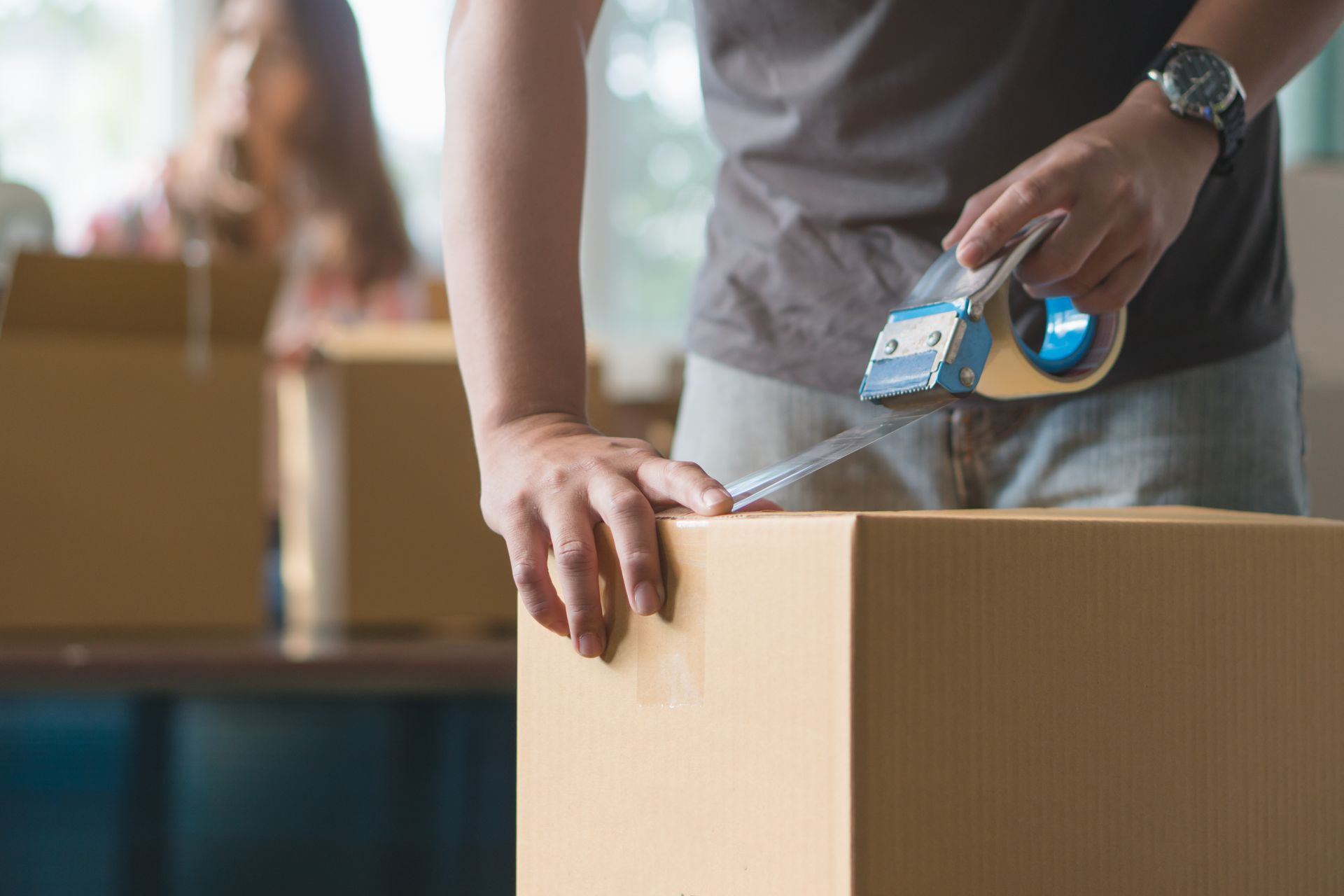 Close-up of a man's hand using tape to seal a cardboard box during a young couple's house-moving process.