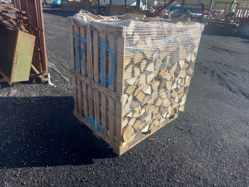 Una cassa piena di legna da ardere accatastata, avvolta in una rete di plastica e appoggiata sull'asfalto.