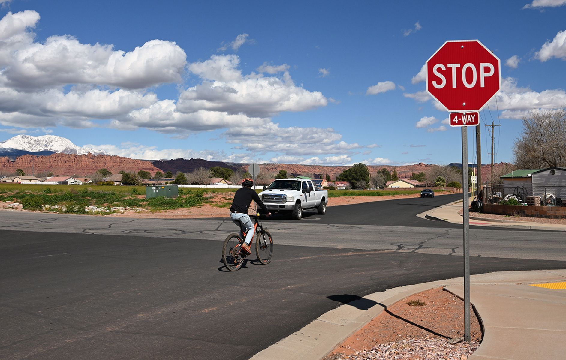 Bicycle rider at intersection with stop sign and car. Bicyclist practicing the stop-as-yield law