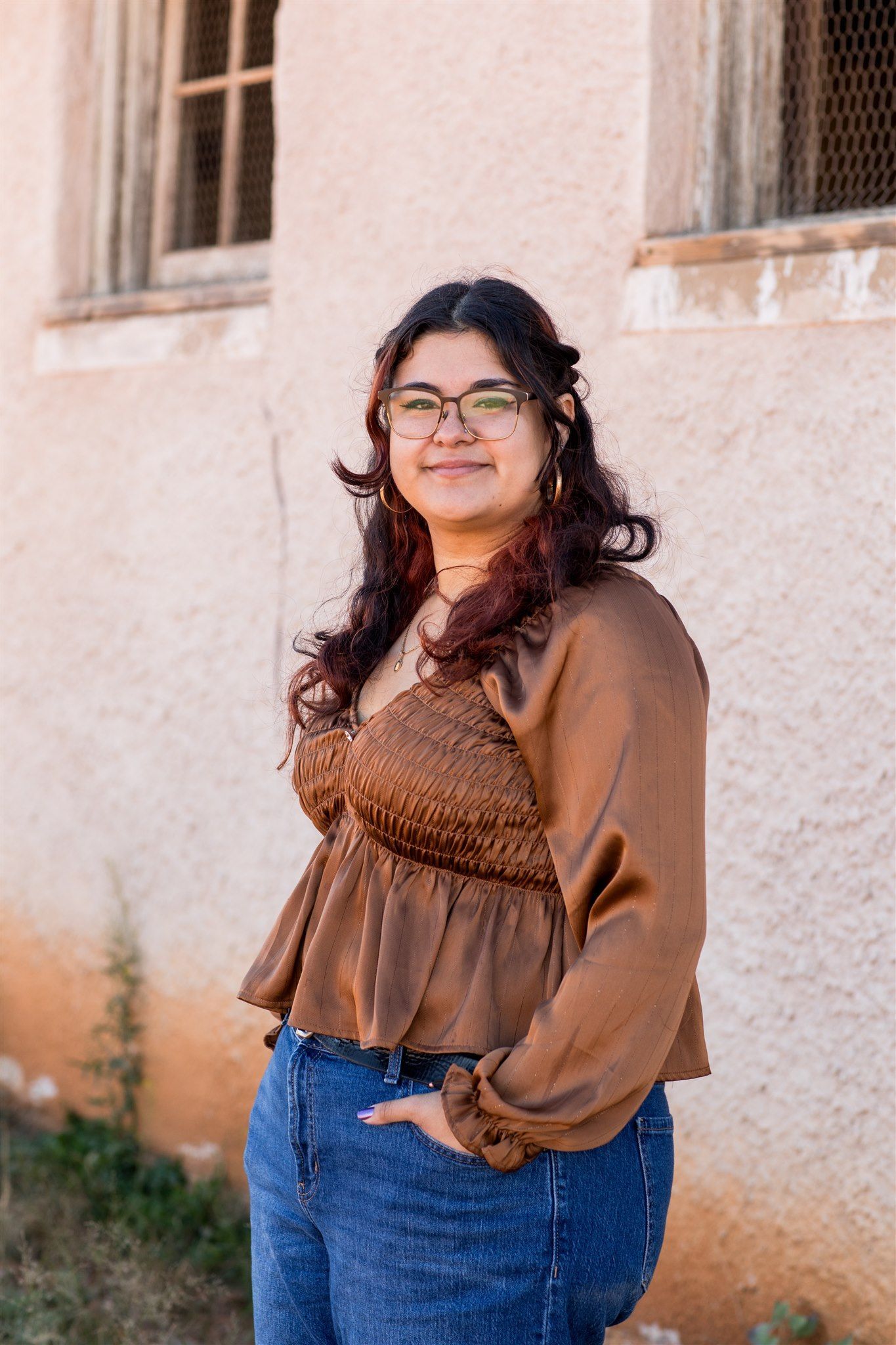 Woman with glasses, red lipstick, and dark curly hair; a close-up shot indoors, looking at the camera.