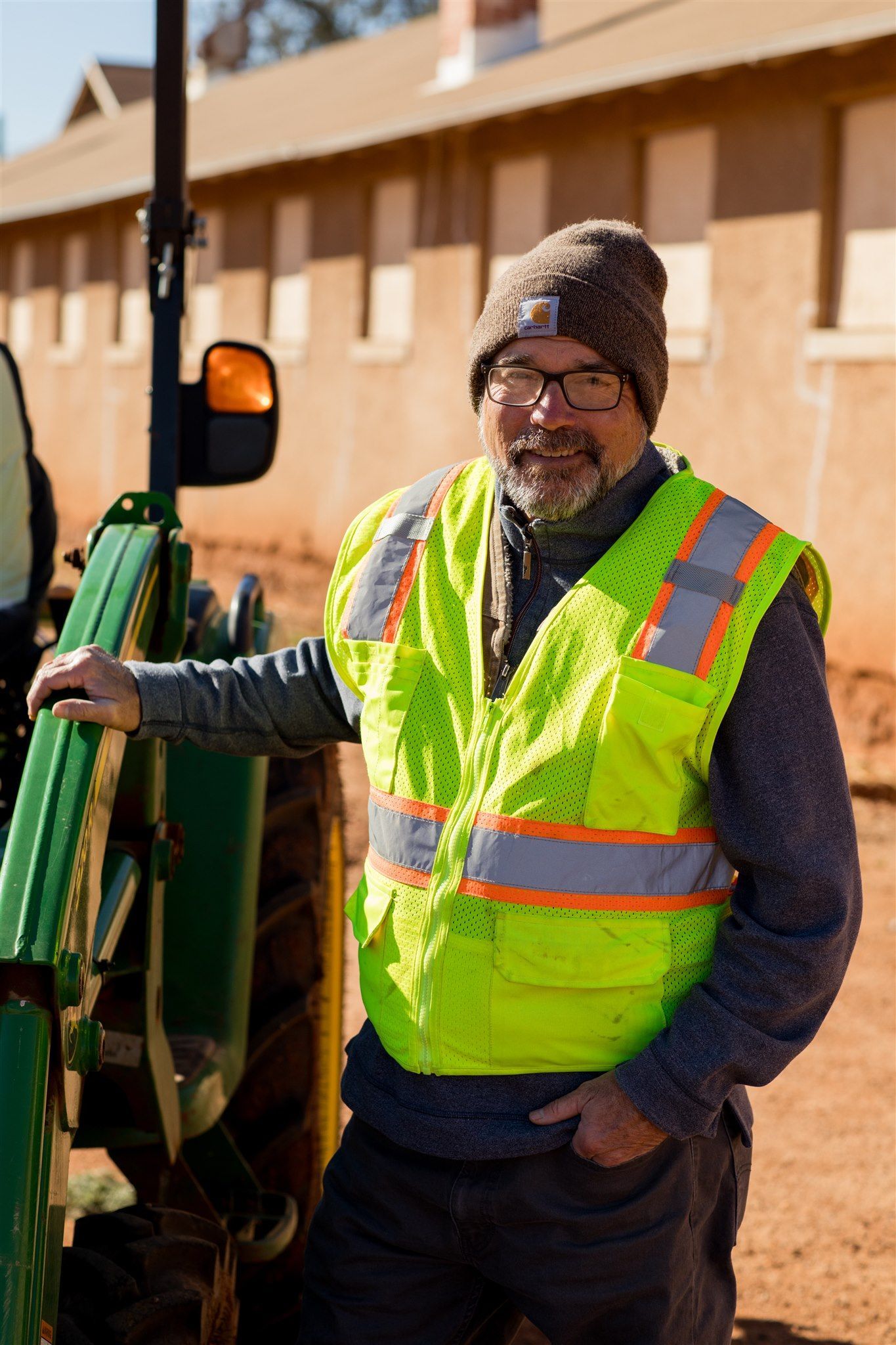 Man with beard and sunglasses smiling in front of a blue sea. He wears a maroon shirt.