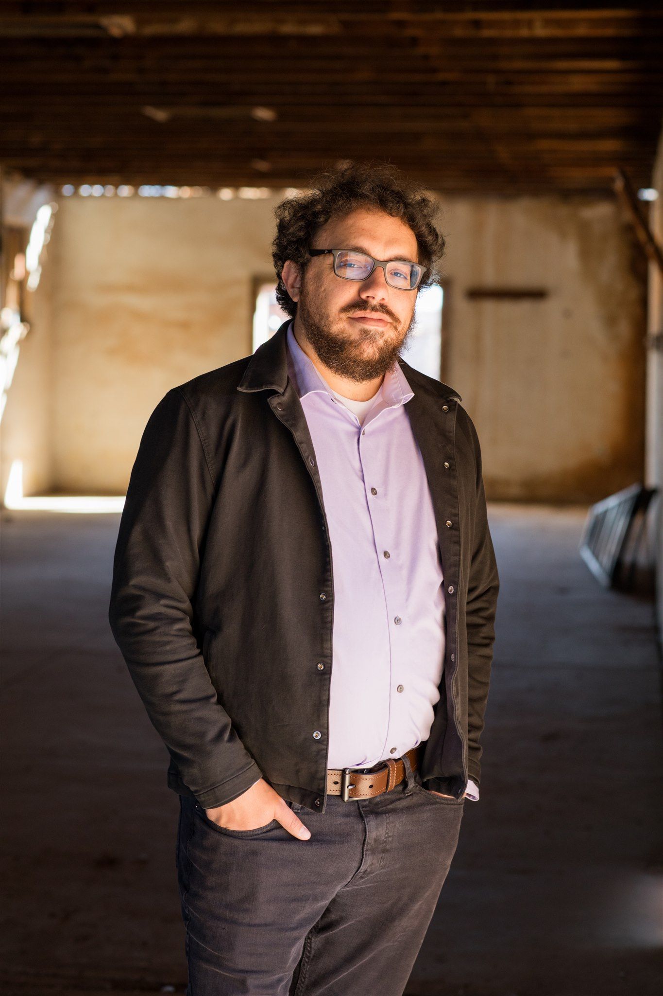 Man with glasses and beard smiles, purple background.
