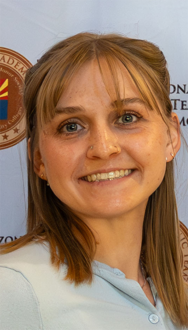 Woman with light brown hair smiles, blue-grey top. Background is a seal with text.