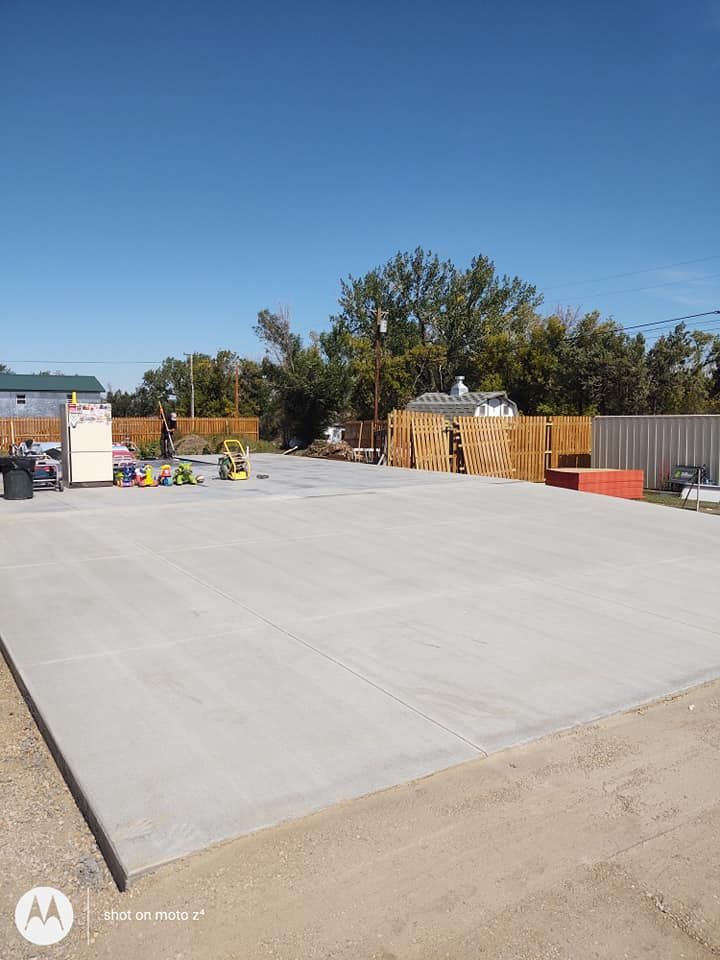 Empty concrete slab at a construction site with fencing, materials, and a clear blue sky