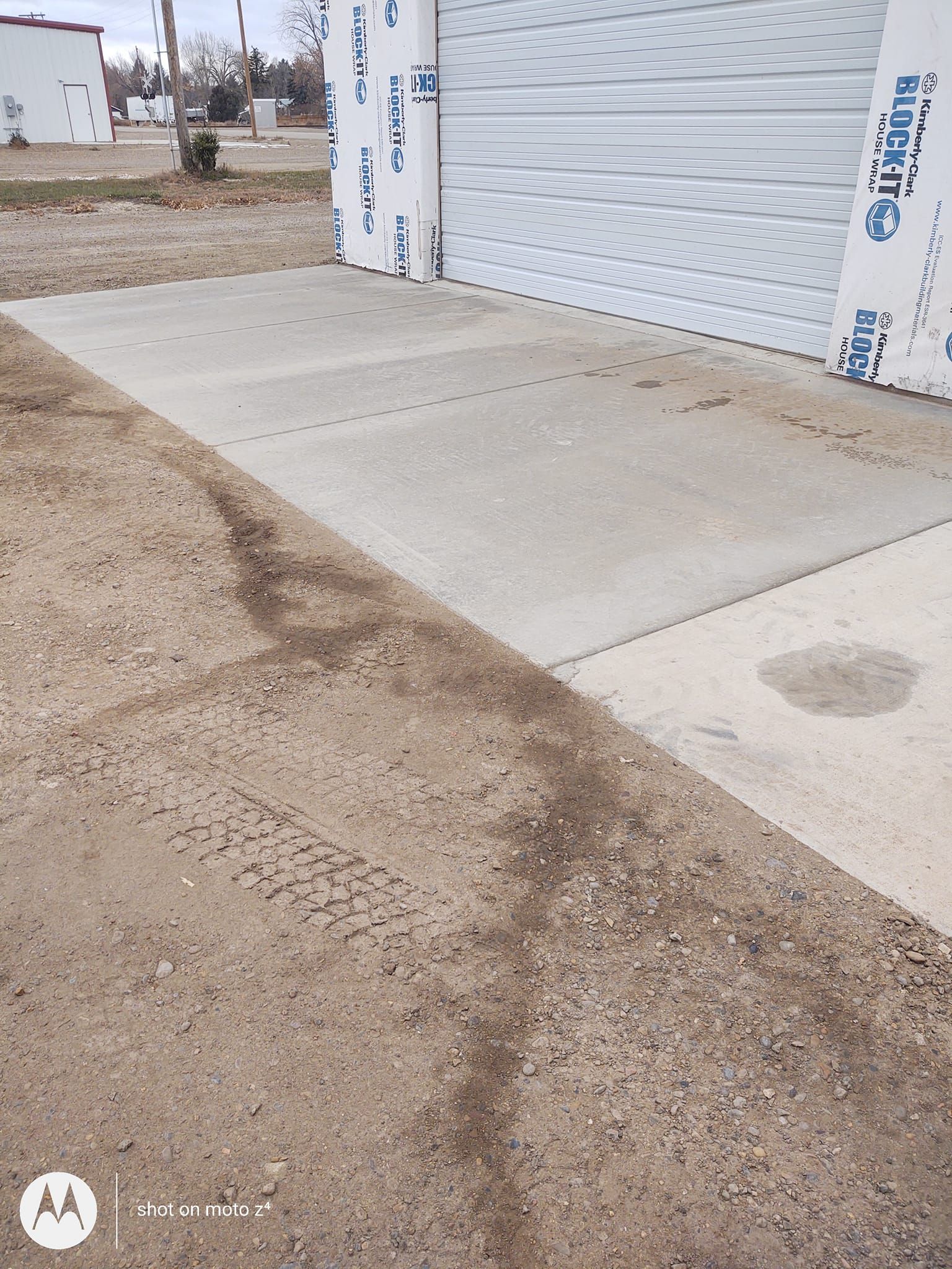 Concrete sidewalk ramp leading to a metal roll-up door beside a dirt lot