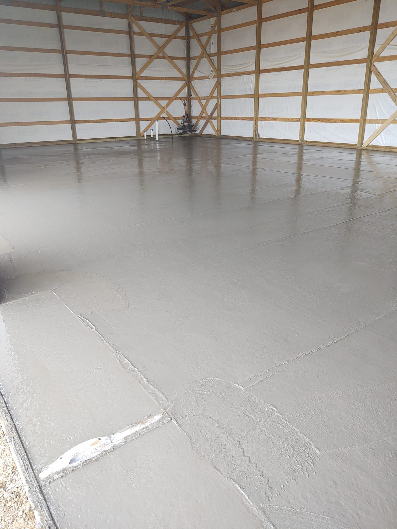 Empty warehouse with a smooth gray concrete floor and a wooden frame wall in the background