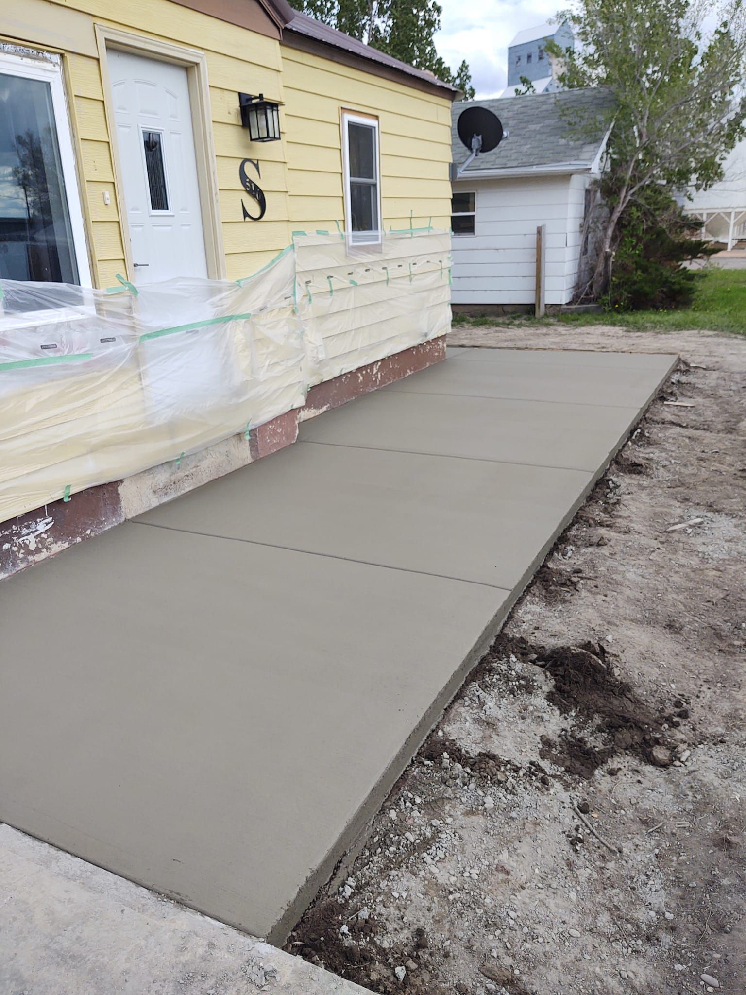 Freshly poured concrete walkway beside a yellow house with white railings and steps