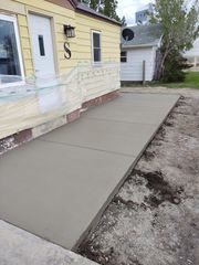 Concrete sidewalk ramp beside a yellow house with white railings and a garage driveway.