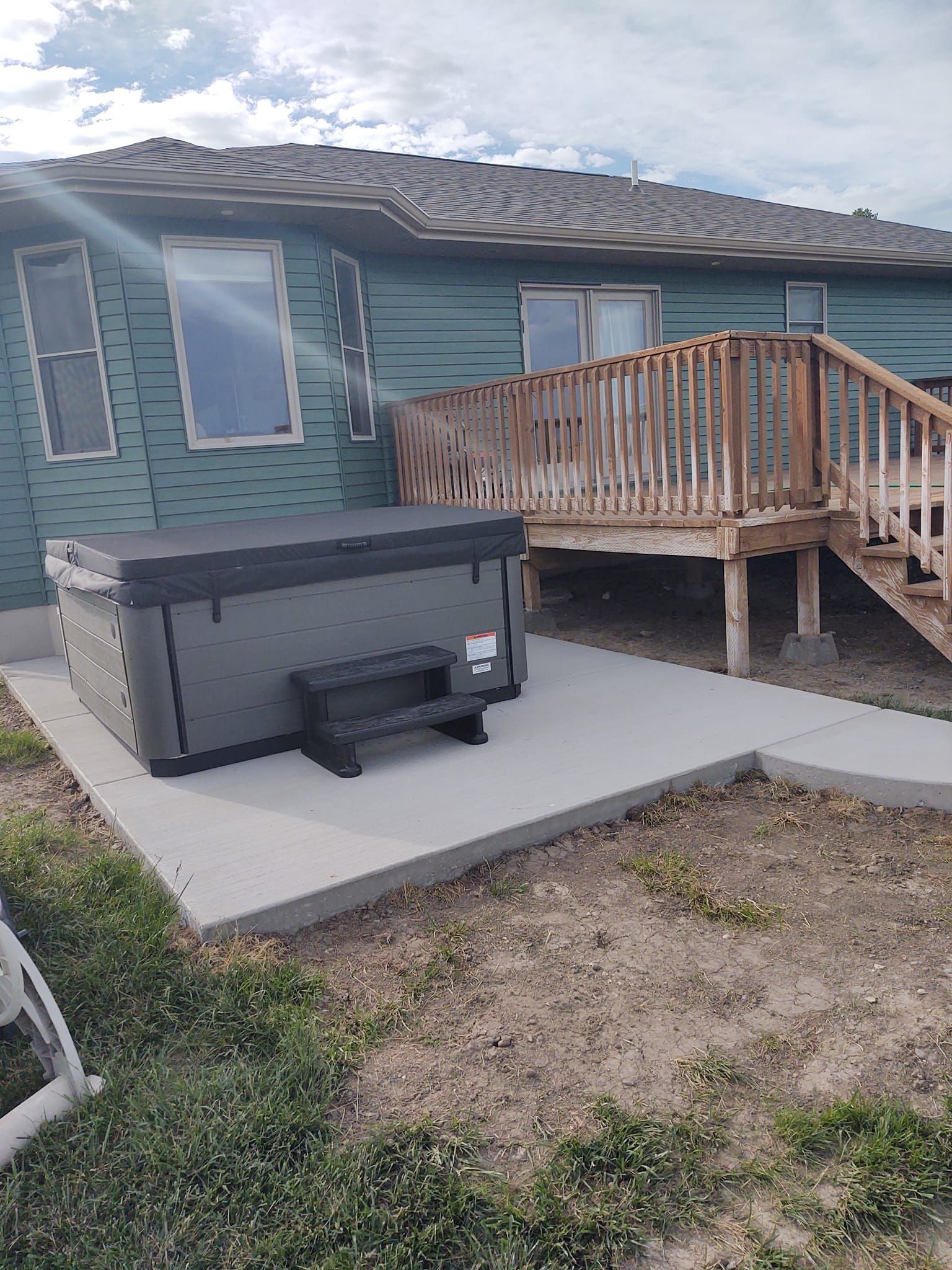 Backyard patio with a hot tub beside a wooden deck attached to a teal house