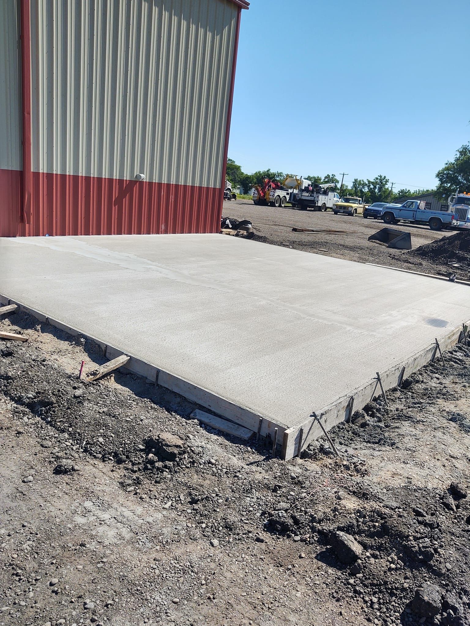 Concrete slab beside red-and-gray metal building in a gravel lot under a clear blue sky