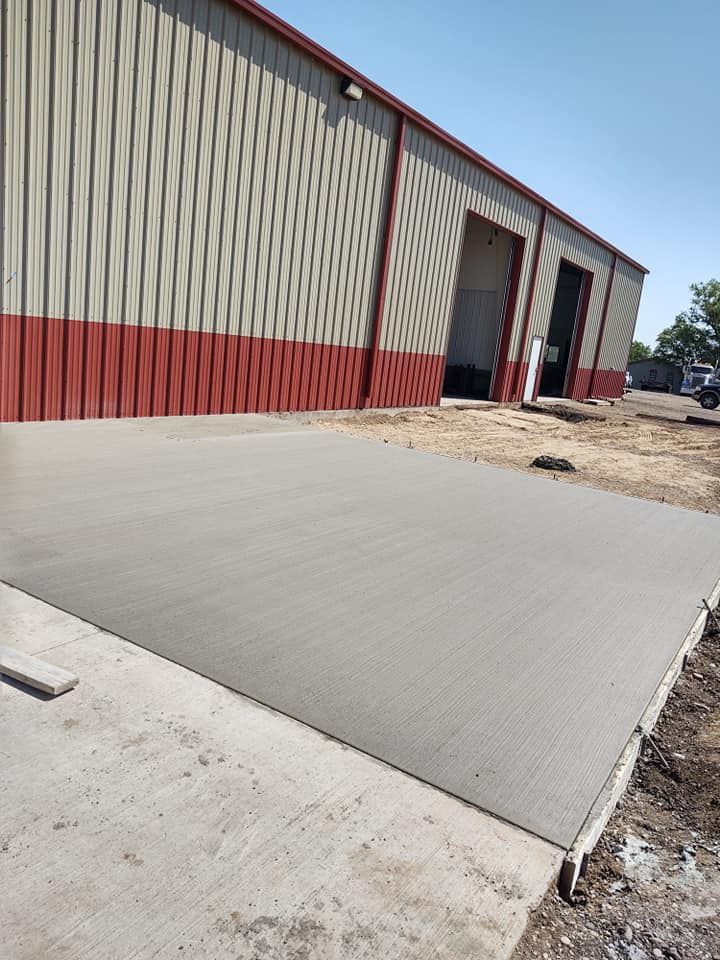 Concrete driveway ramp beside a red and beige industrial warehouse under construction
