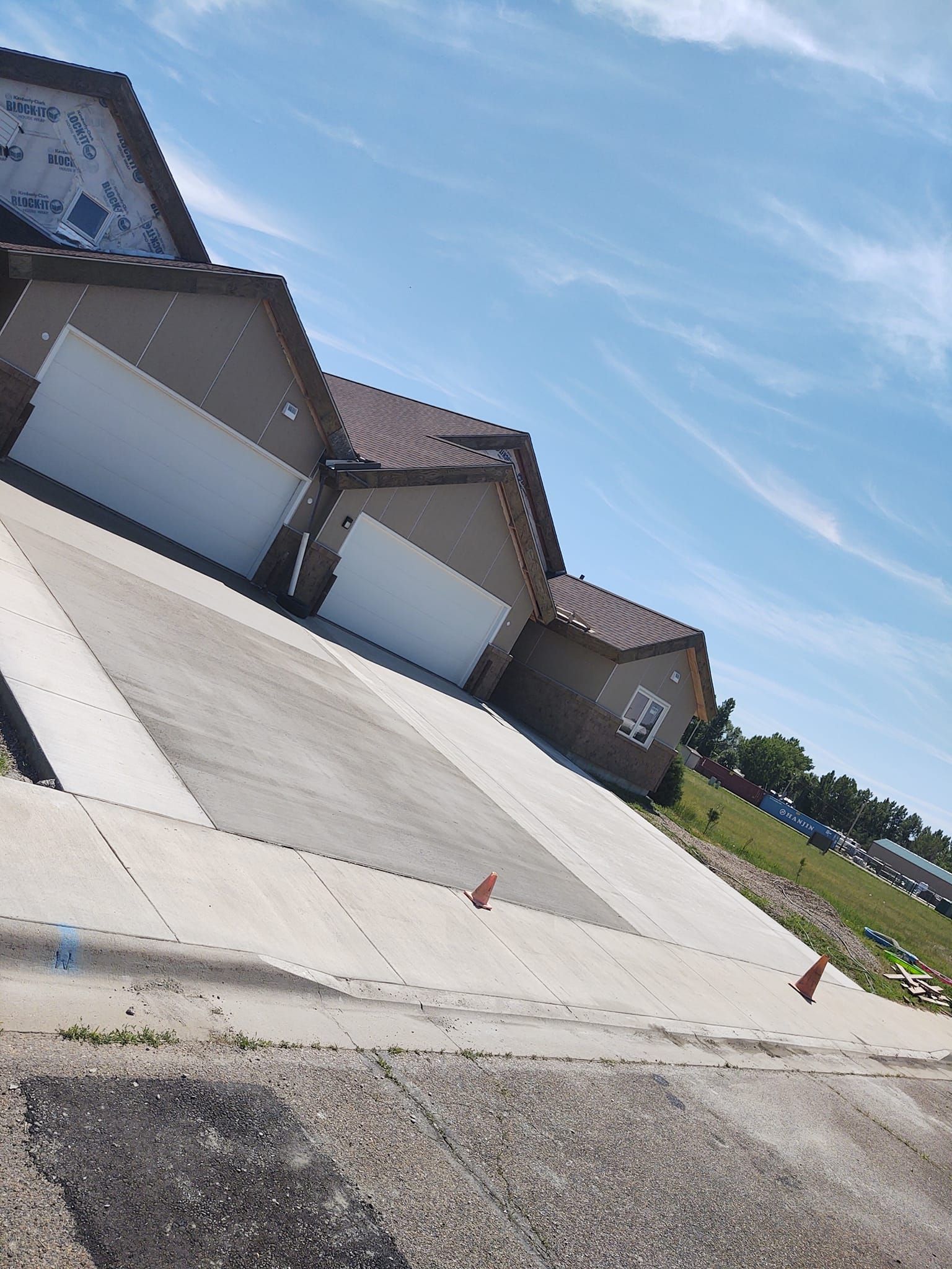 Tilted view of a row of beige garage doors beside a concrete driveway under a blue sky