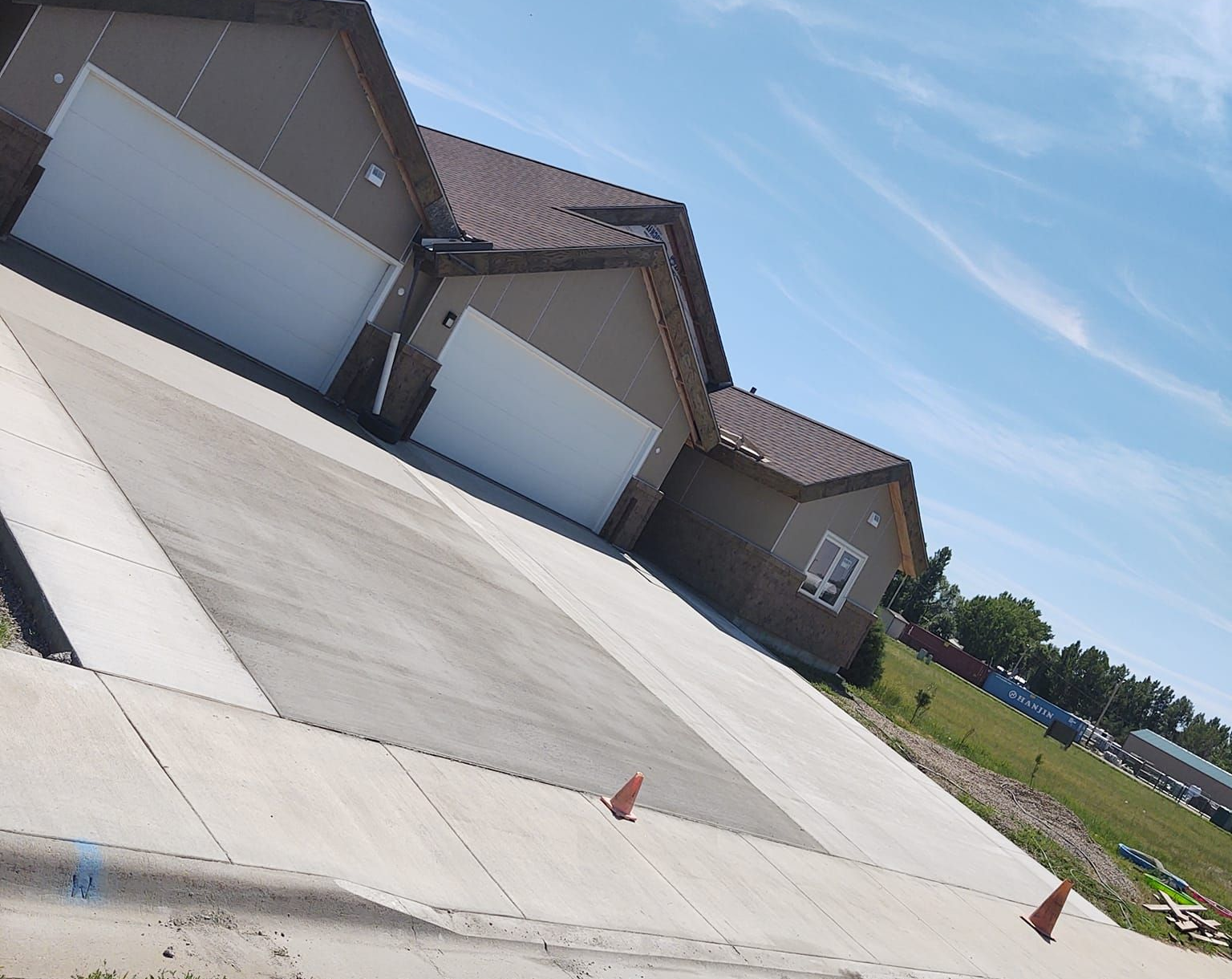 Tilted view of a suburban house with three garage doors and a wide concrete driveway under a blue sky