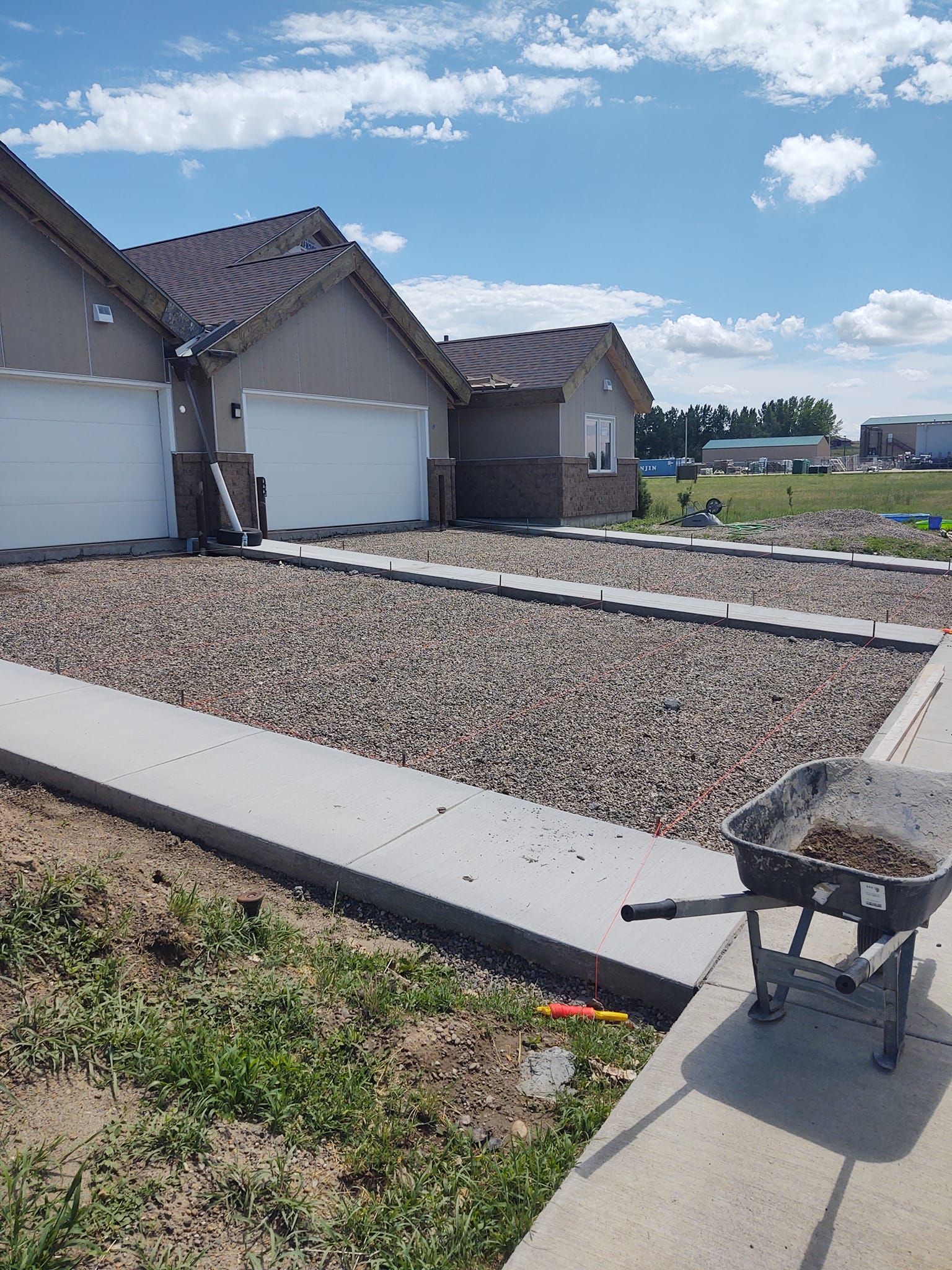 Suburban house with garage, xeriscaped front yard, and a wheelbarrow on the sidewalk under a blue sky