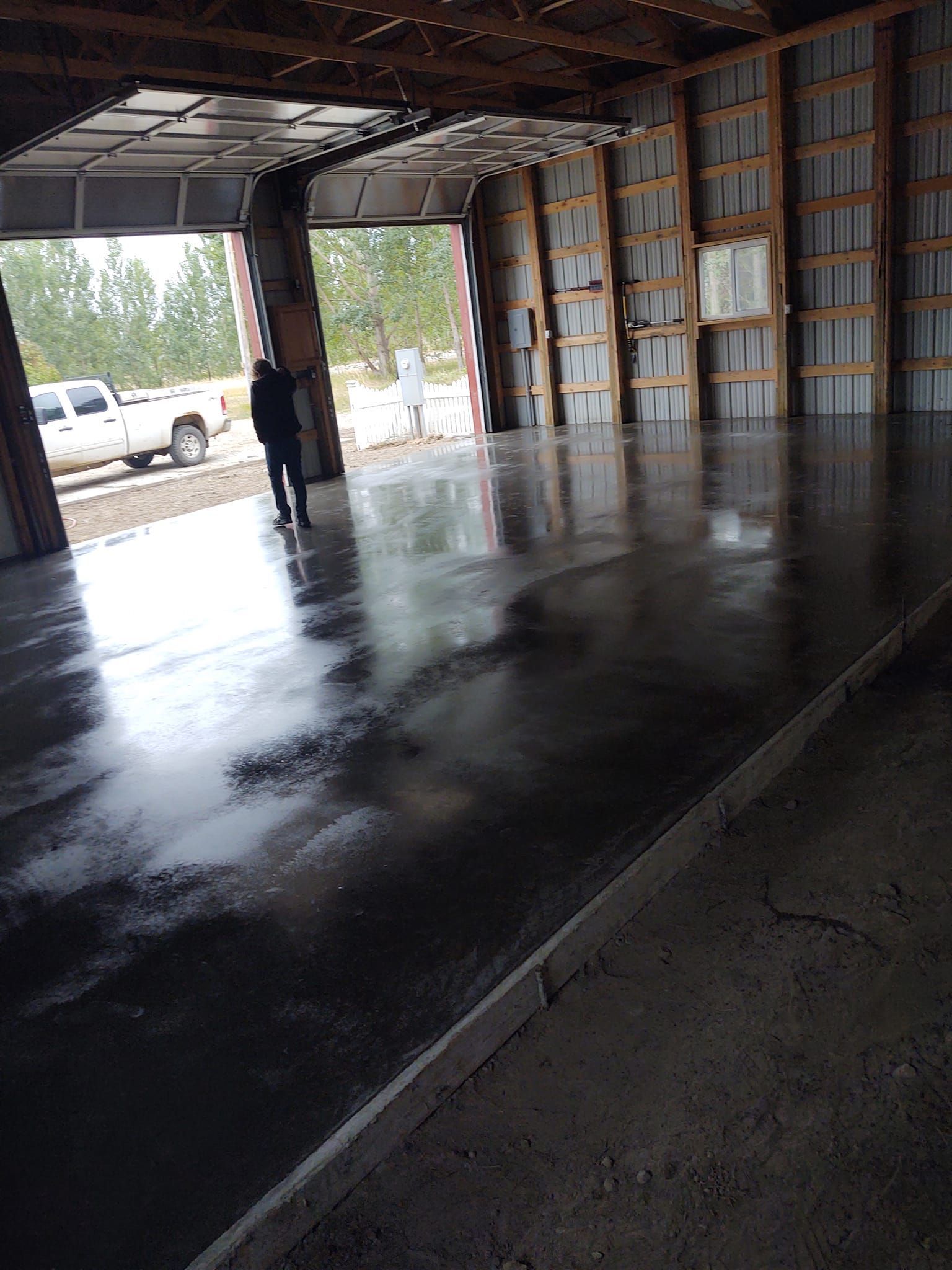 Empty warehouse interior with a wet, reflective concrete floor and open loading bay doors.