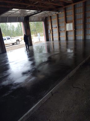 Dim warehouse interior with a wet concrete floor and a person standing near the open doorway.