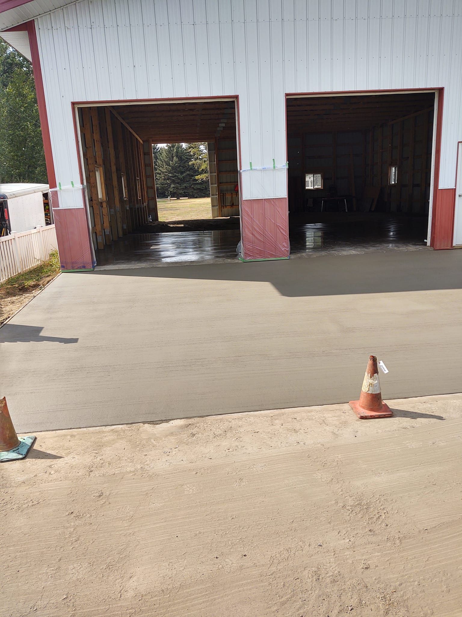 Two open garage bays in a white building with orange traffic cones in front of a freshly paved driveway.