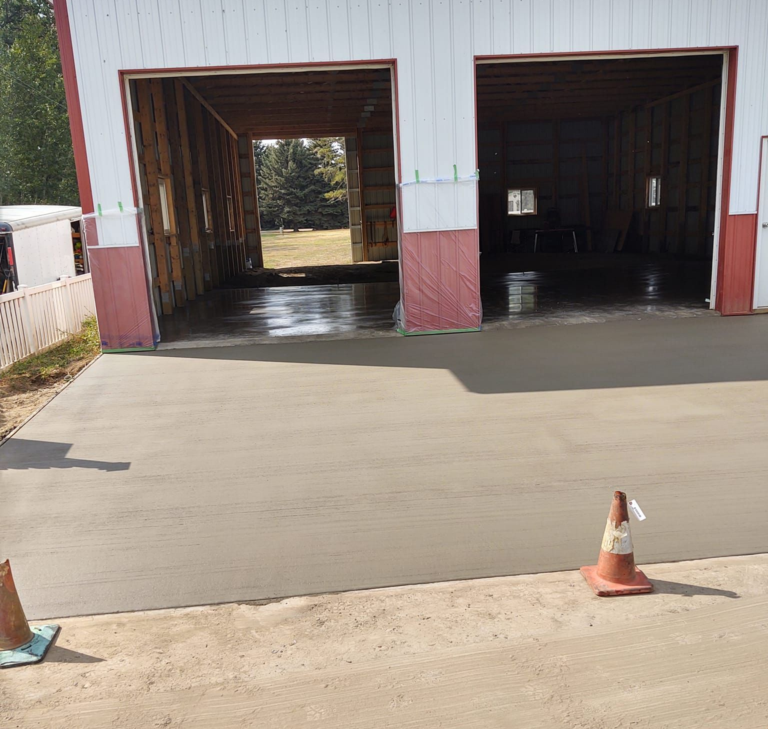 Open garage bays in a white and red building, with a freshly paved driveway and traffic cones in front