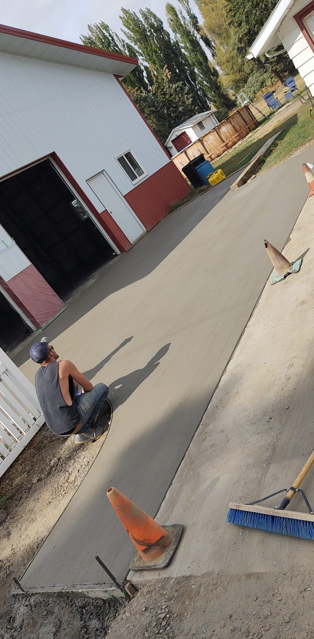 Tilted view of an outdoor worksite with a person kneeling by a building, traffic cones, and construction materials.