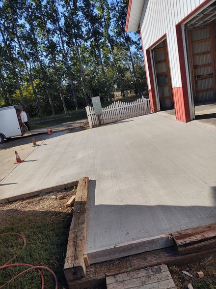 Concrete driveway leading to an open garage, with a red-and-white house and a white fence in the background.