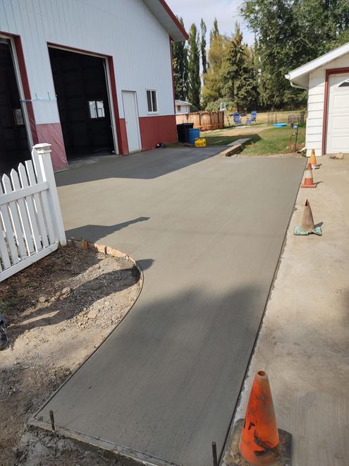 Fresh concrete walkway beside a white building with orange cones marking the path