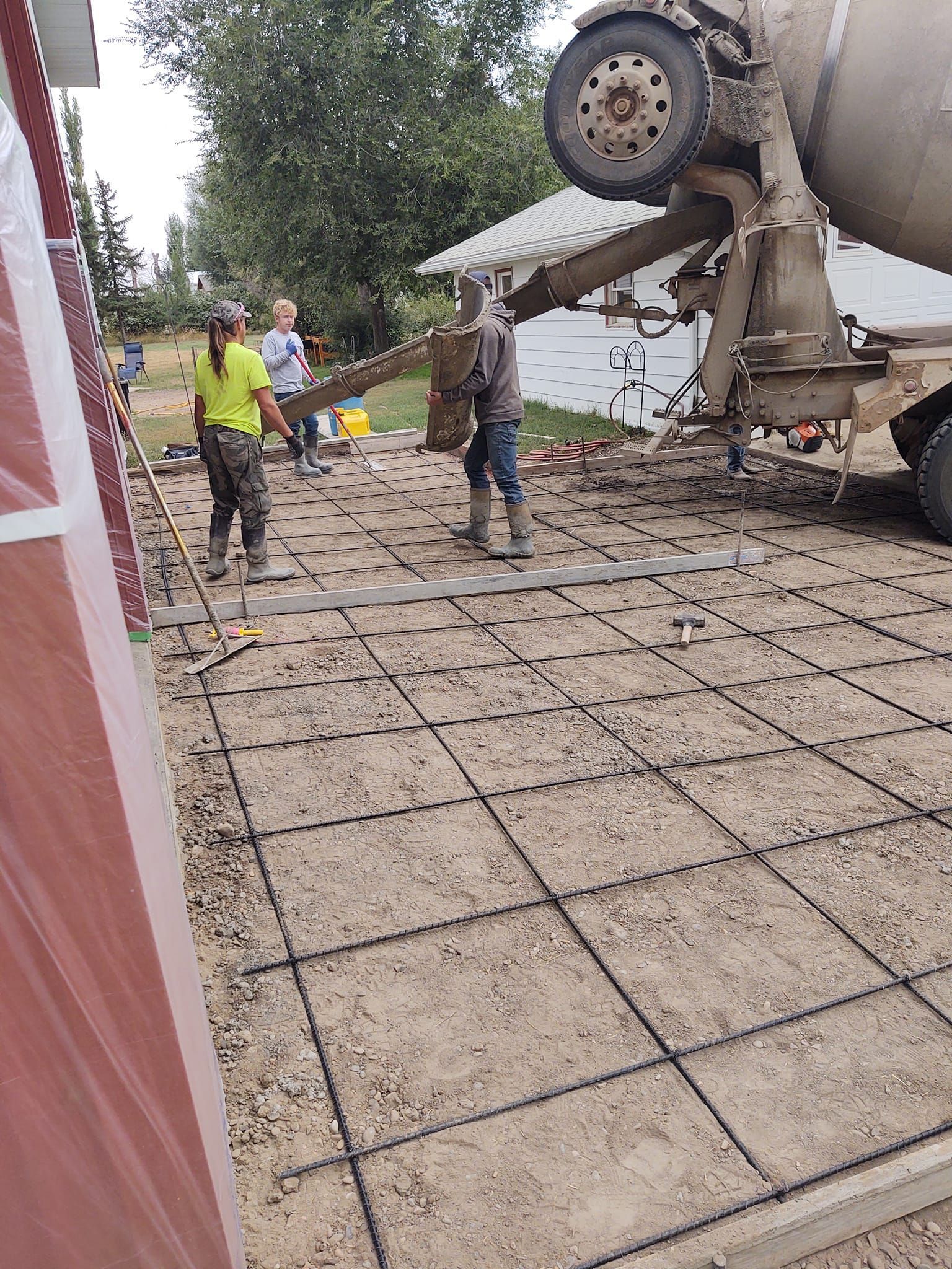 Workers beside a tipped cement mixer on a construction site, with spilled concrete and damaged equipment.