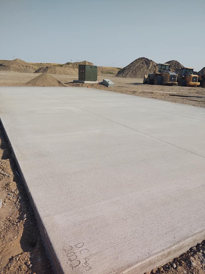 Fresh concrete slab at a construction site with dirt piles and heavy machinery in the background