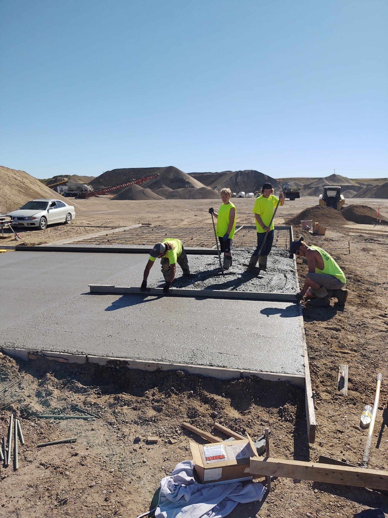 Workers in neon vests installing a concrete slab on a construction site under a clear sky