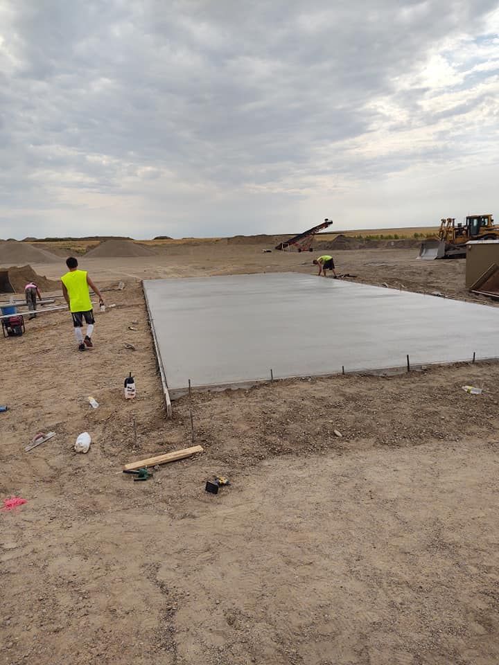 Concrete slab under construction on a dusty site, with workers and heavy equipment in the background.