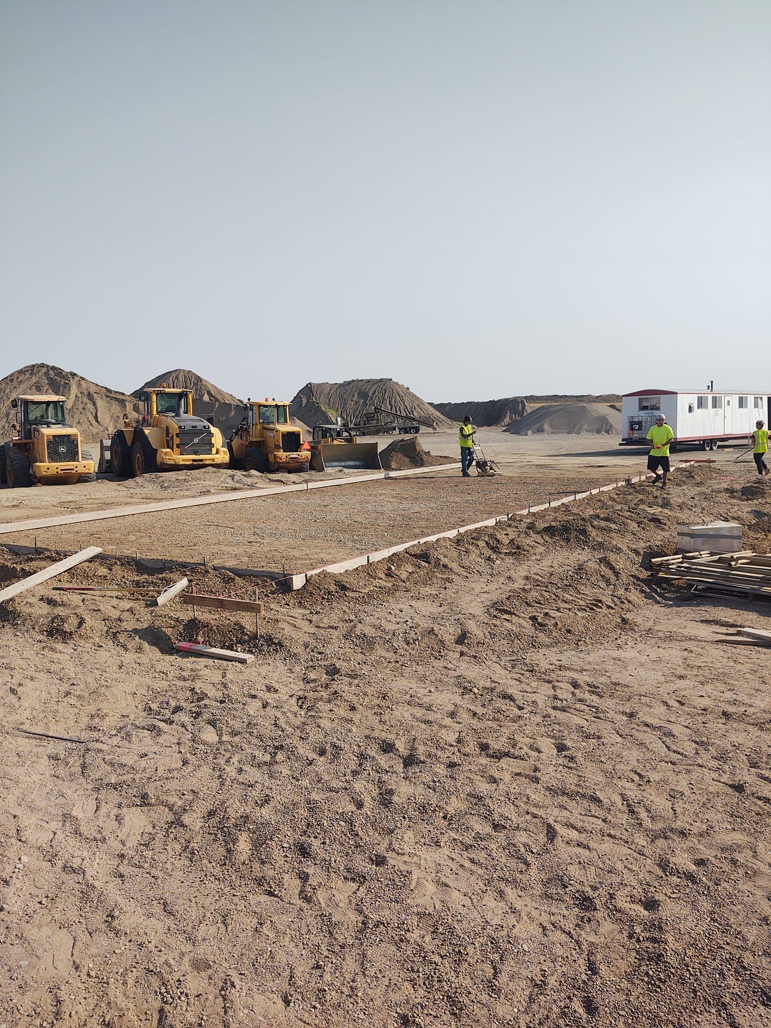 Construction site with several excavators grading a dirt lot under a clear sky, workers nearby and a utility truck on the right