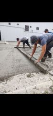 Workers smoothing wet concrete at a construction site with a long straightedge.