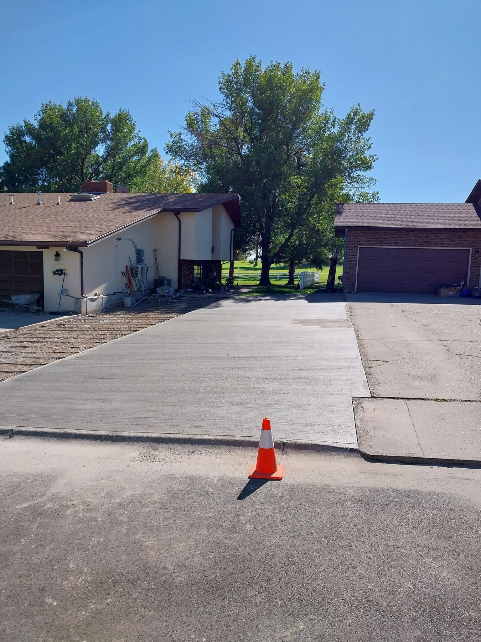 Driveway between two houses on a sunny day, with an orange traffic cone in the foreground.