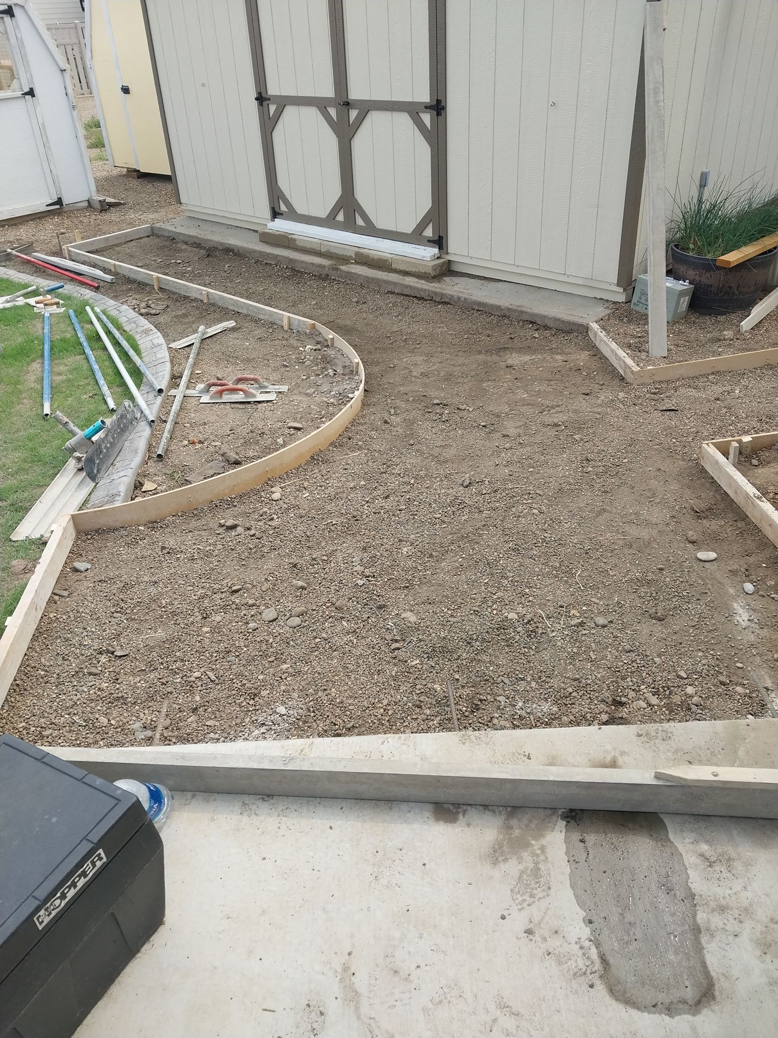 Backyard gravel path under construction beside a white shed and patio edge