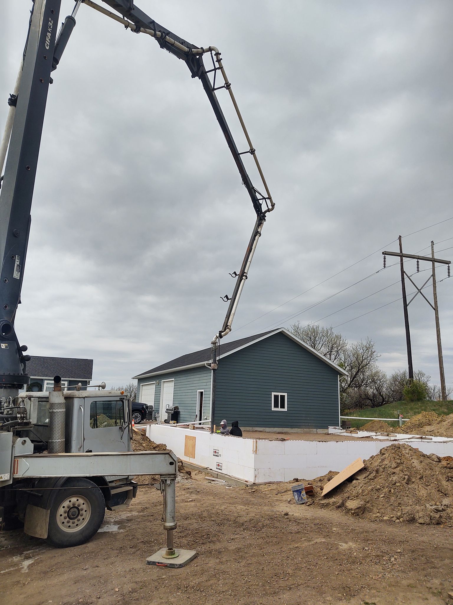 Concrete pump boom pouring into a new house foundation on a cloudy construction site.