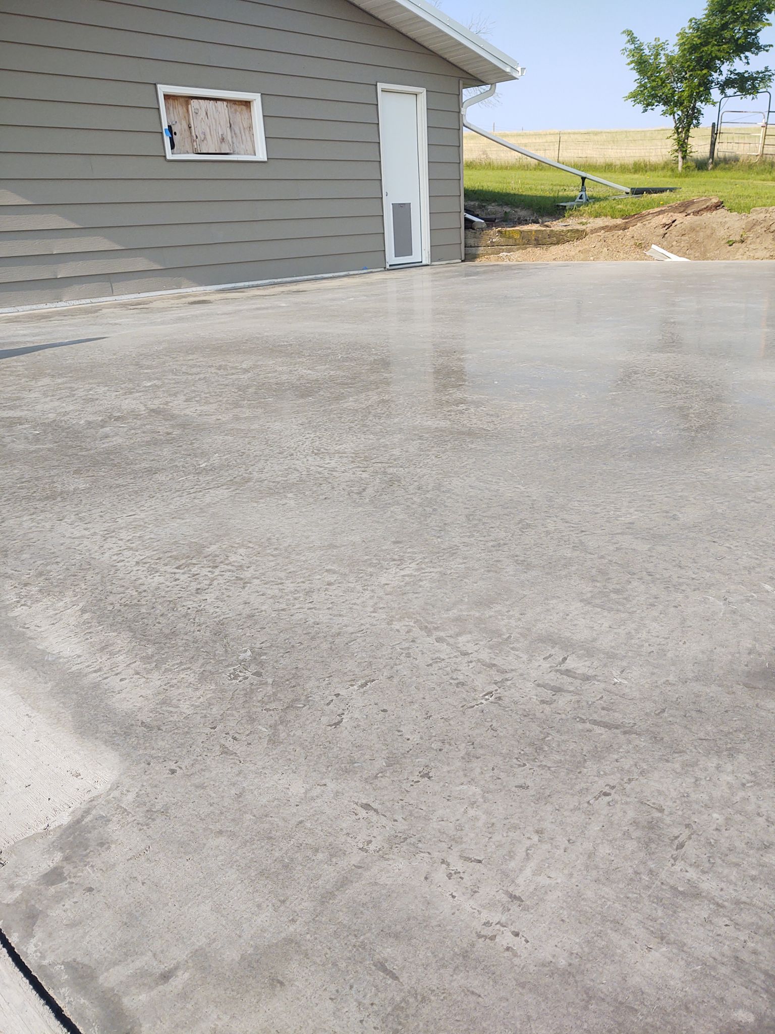 Gravel driveway beside a gray house with a white door, overlooking a grassy field.