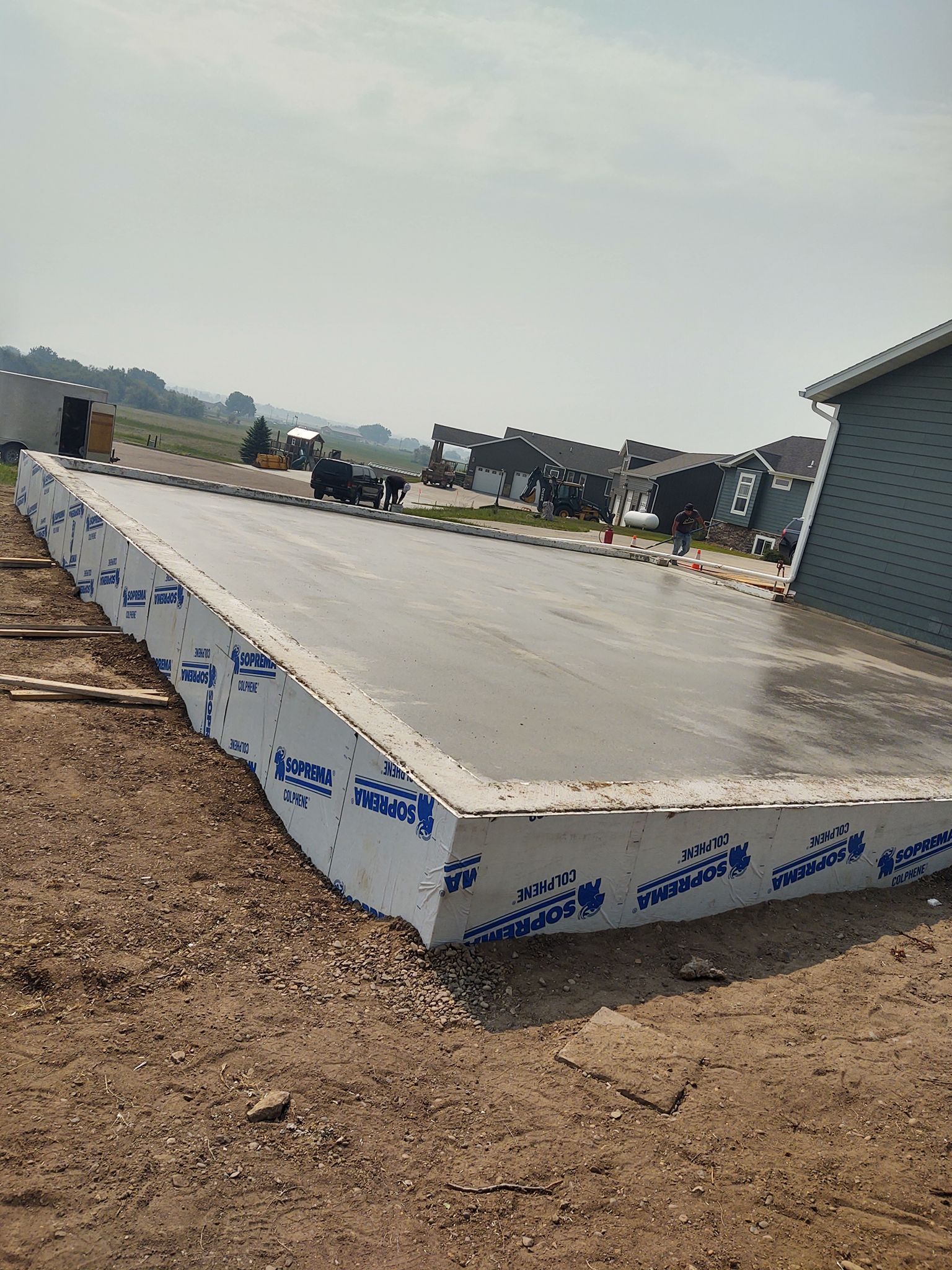 Concrete slab foundation under construction, wrapped in white insulation, at a building site.