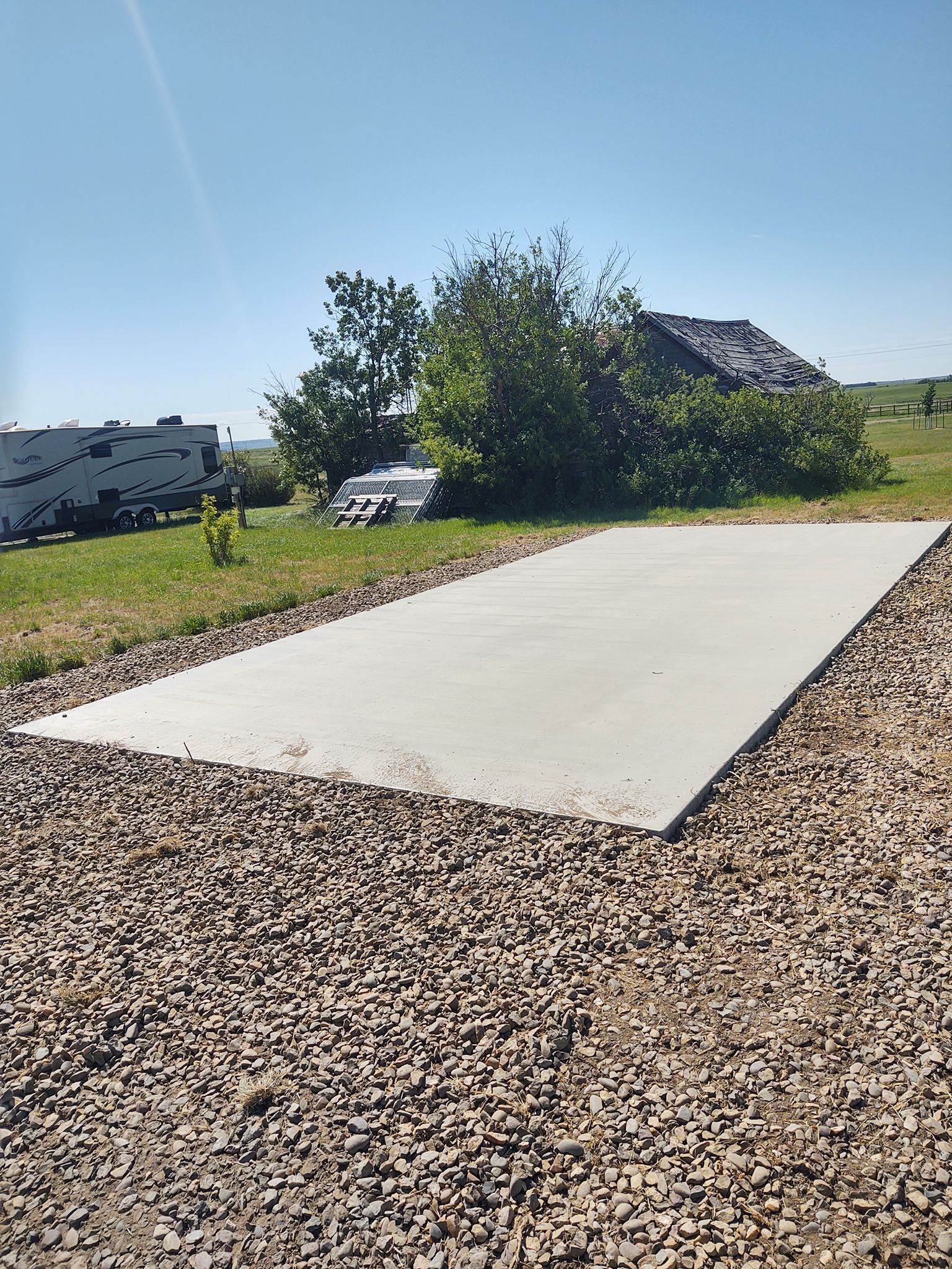 Outdoor concrete slab beside gravel and grass under a sunny blue sky