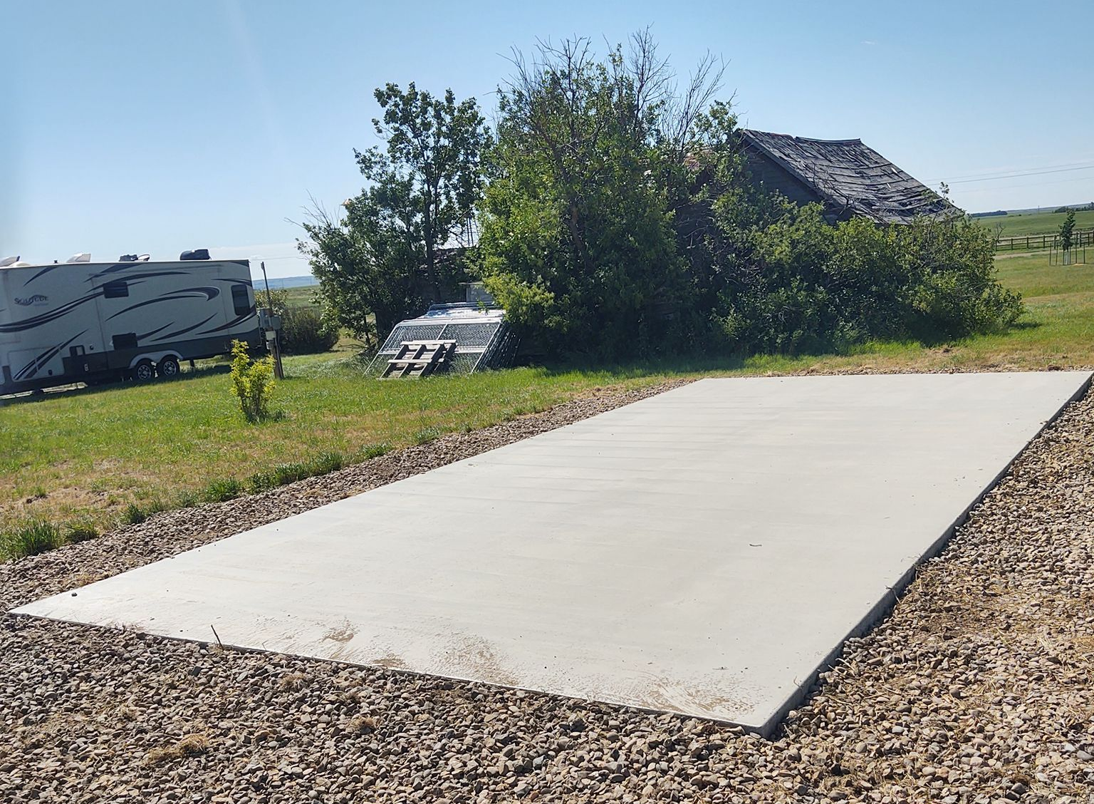 Concrete RV pad in a grassy field with an RV and house in the background