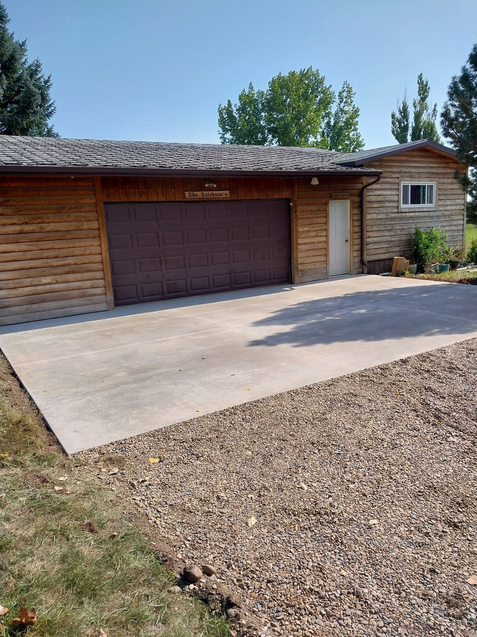 Single-story house with a garage, concrete driveway, and gravel yard under a blue sky