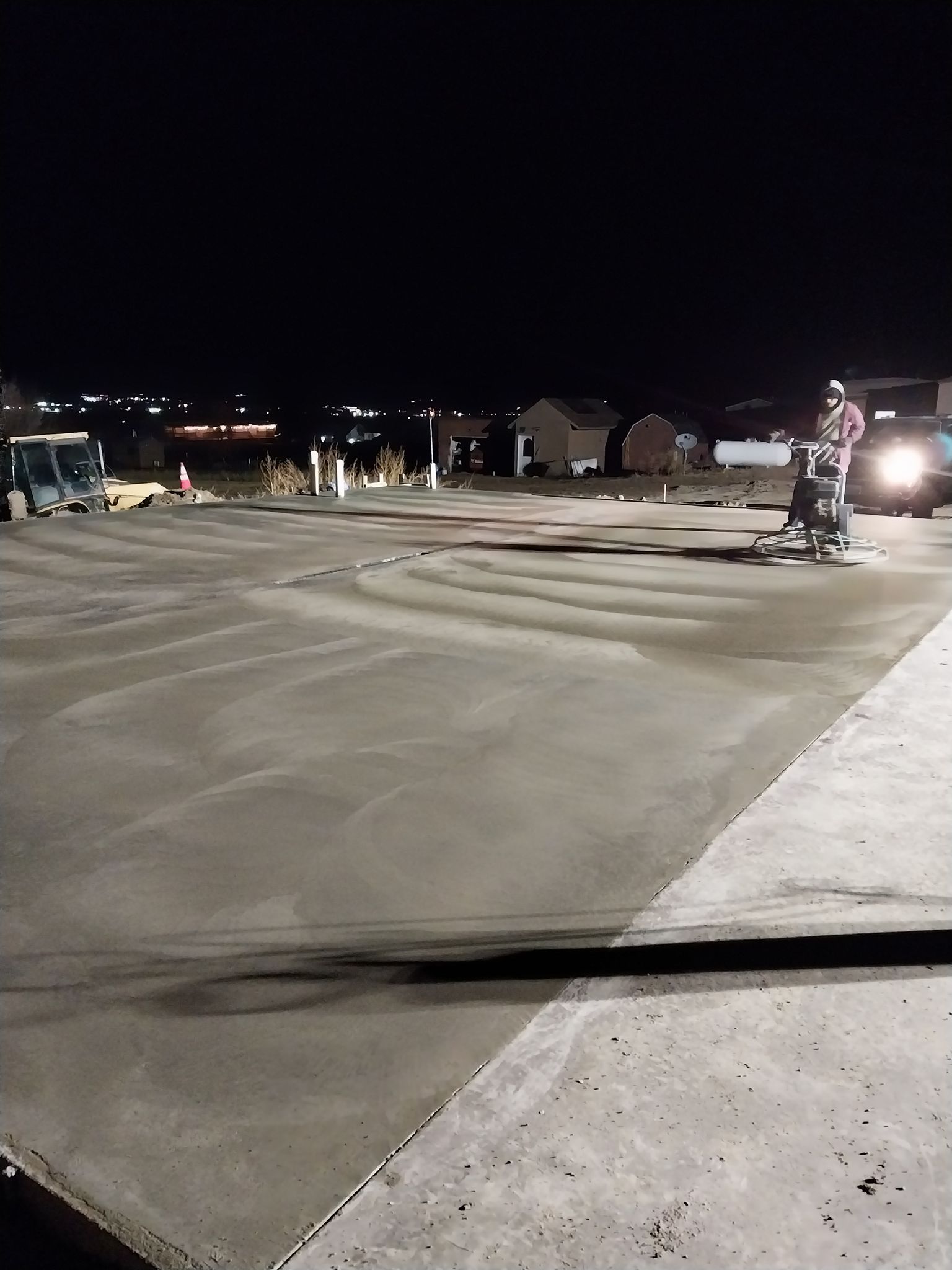 Snow-covered parking lot at night with vehicles and bright headlights illuminating the scene.