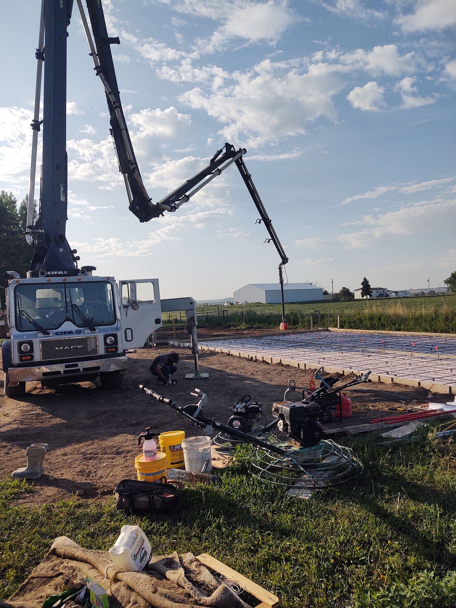 Concrete pump truck pouring concrete at a roadside construction site under a cloudy sky