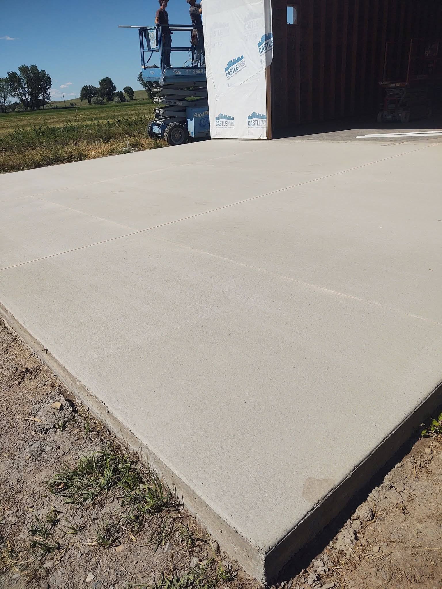 Concrete slab beside an open industrial building on a sunny day with fields in the background