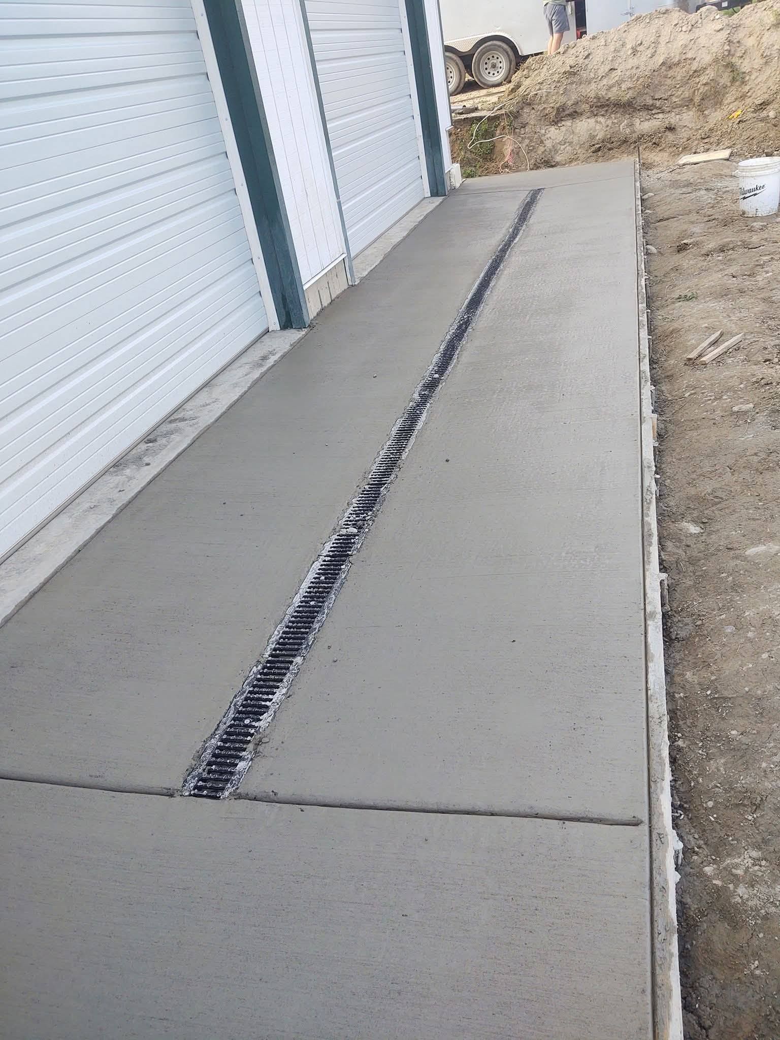 Concrete walkway beside a garage with a long center drainage channel and dirt yard