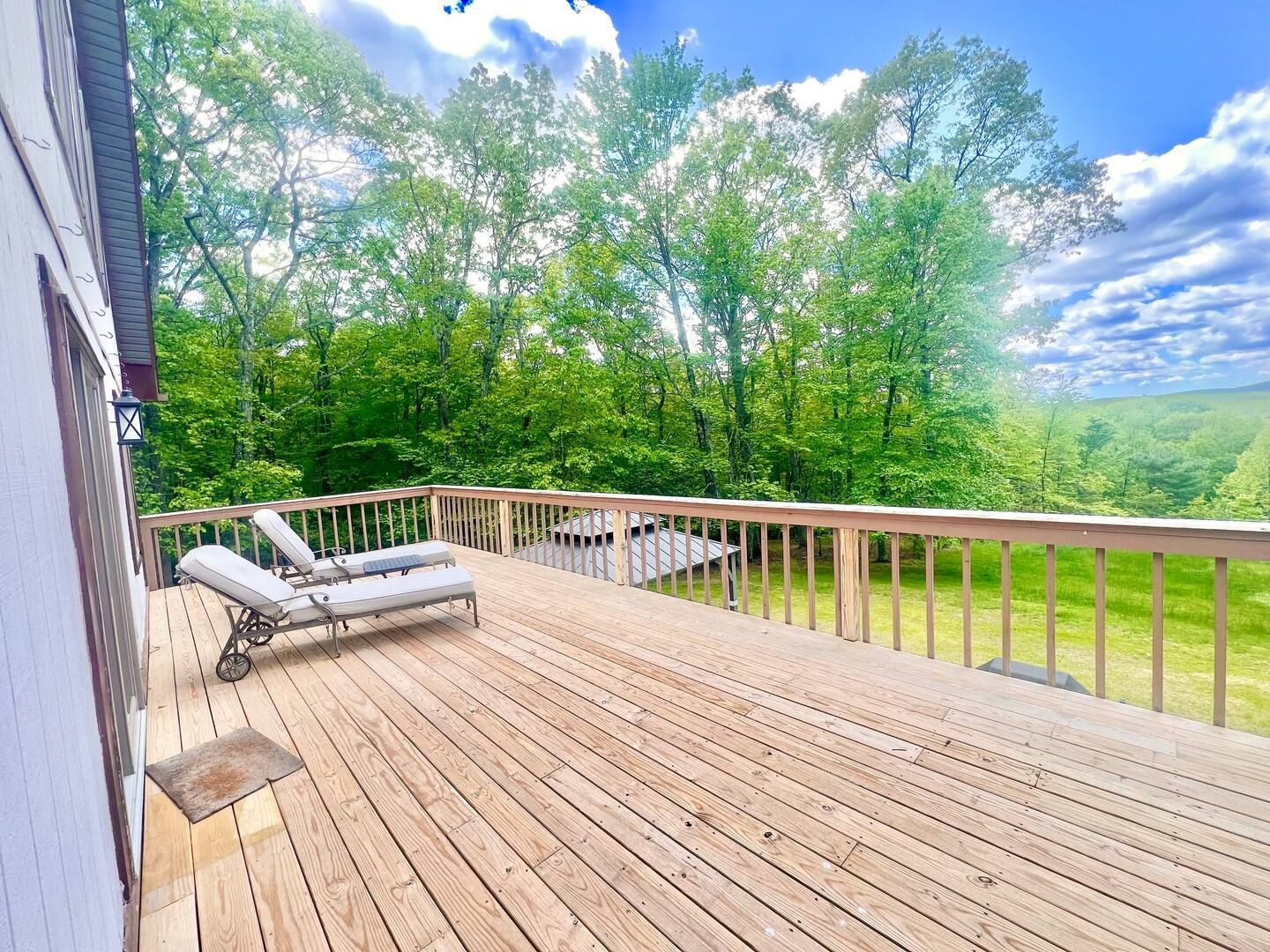Wooden deck with two lounge chairs, overlooking a forest.