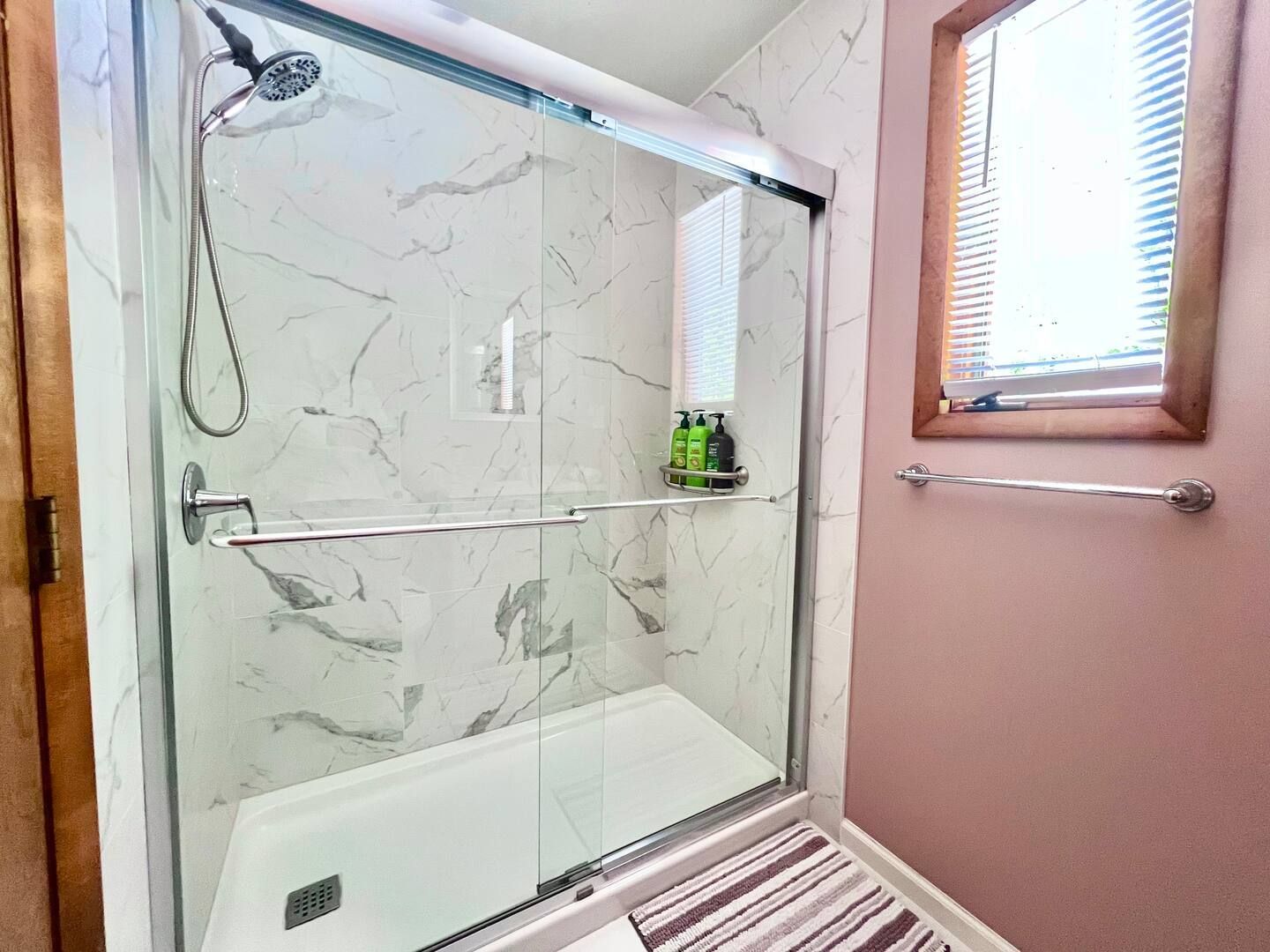Shower with marble-patterned walls, glass doors, and a window with blinds.