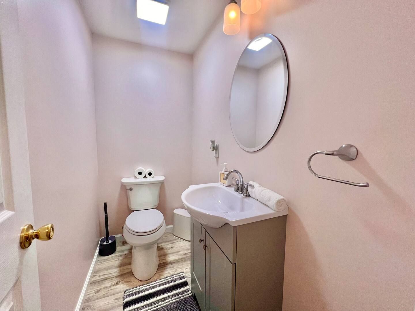 A small bathroom with pink walls, a toilet, sink, and oval mirror.