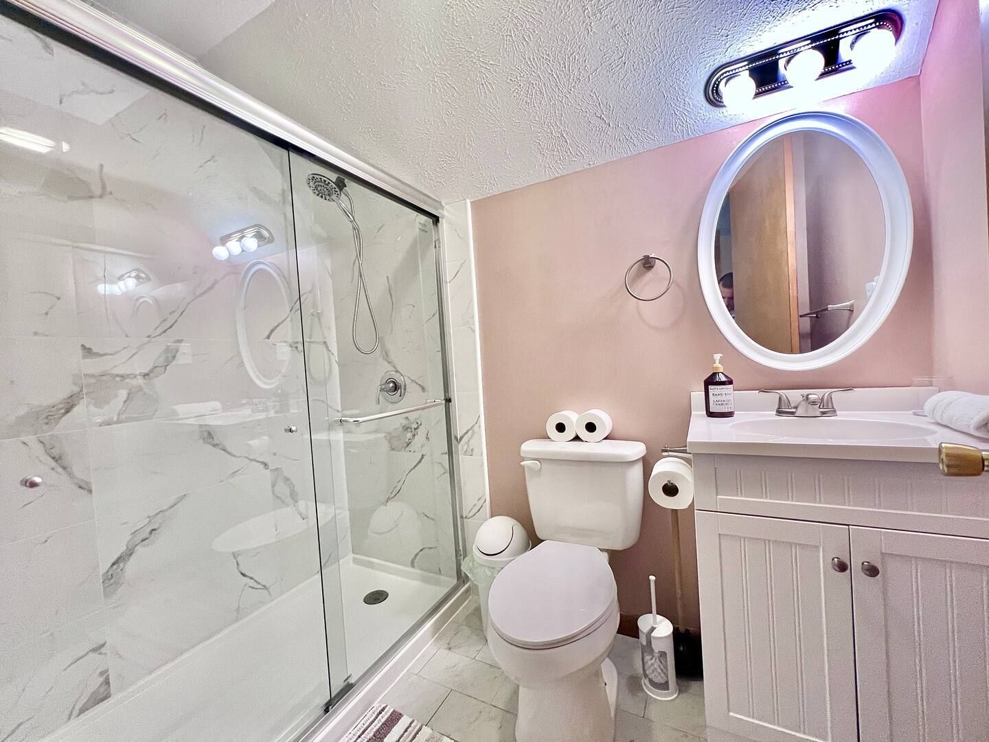 Bathroom with white marble shower, pink walls, and white vanity.