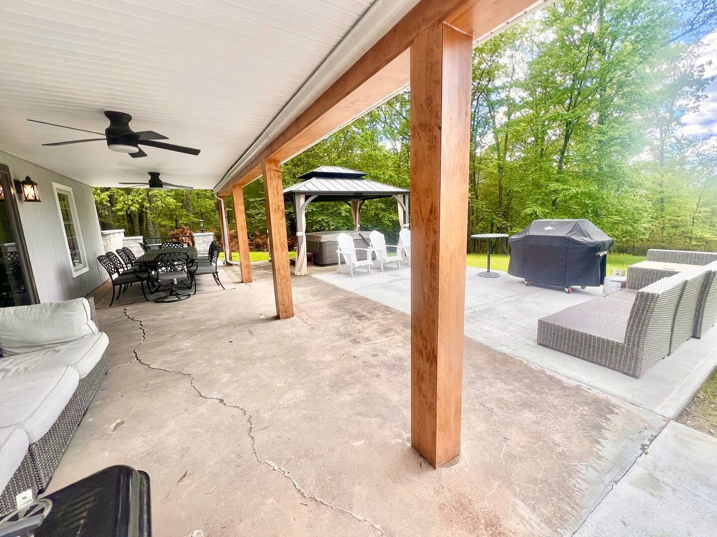 Covered outdoor patio with seating, grill, and gazebo in the background.