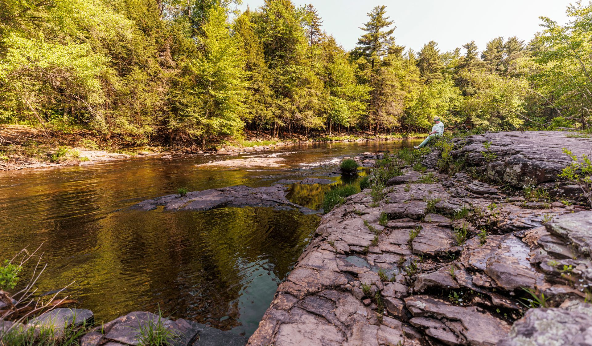 River flowing through a rocky area with trees in the background under a bright sky.