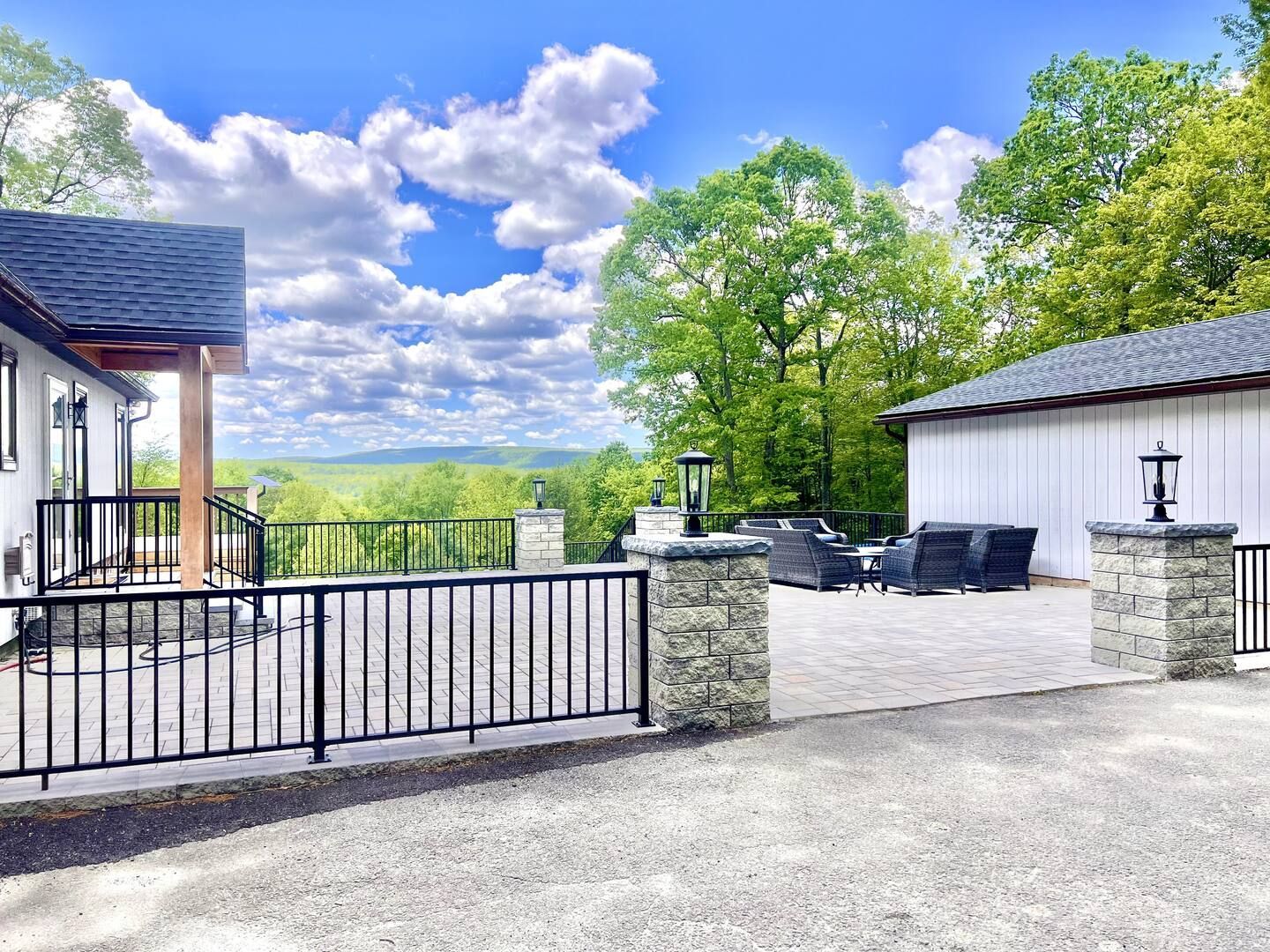 A white house with a patio overlooks a green valley under a blue sky with puffy clouds.